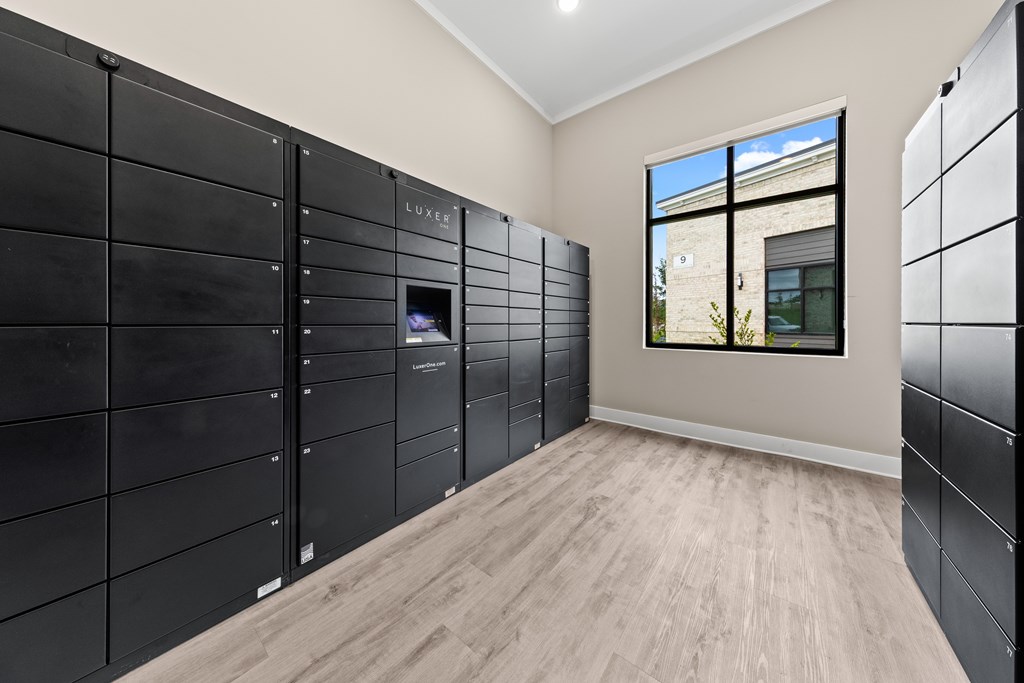 A room with a wall of black lockers and a window showing a building outside at Views at Flowers Apartments, Clayton, NC, 27527