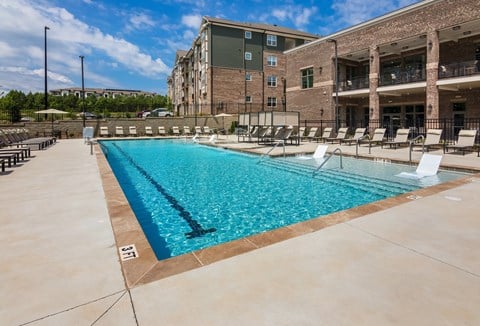 a swimming pool with lounge chairs and umbrellas in front of a brick building  at Ardmore at Bryton, Huntersville, NC, 28078