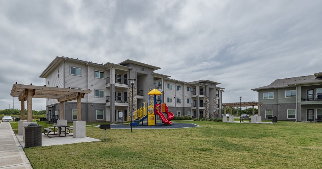 an outdoor play area with a yellow and red slide in front of an apartment building