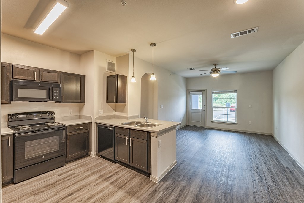 an empty kitchen and living room with wood flooring and a ceiling fan