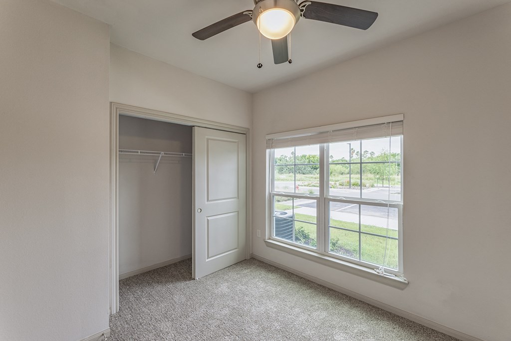 an empty bedroom with a window and a ceiling fan