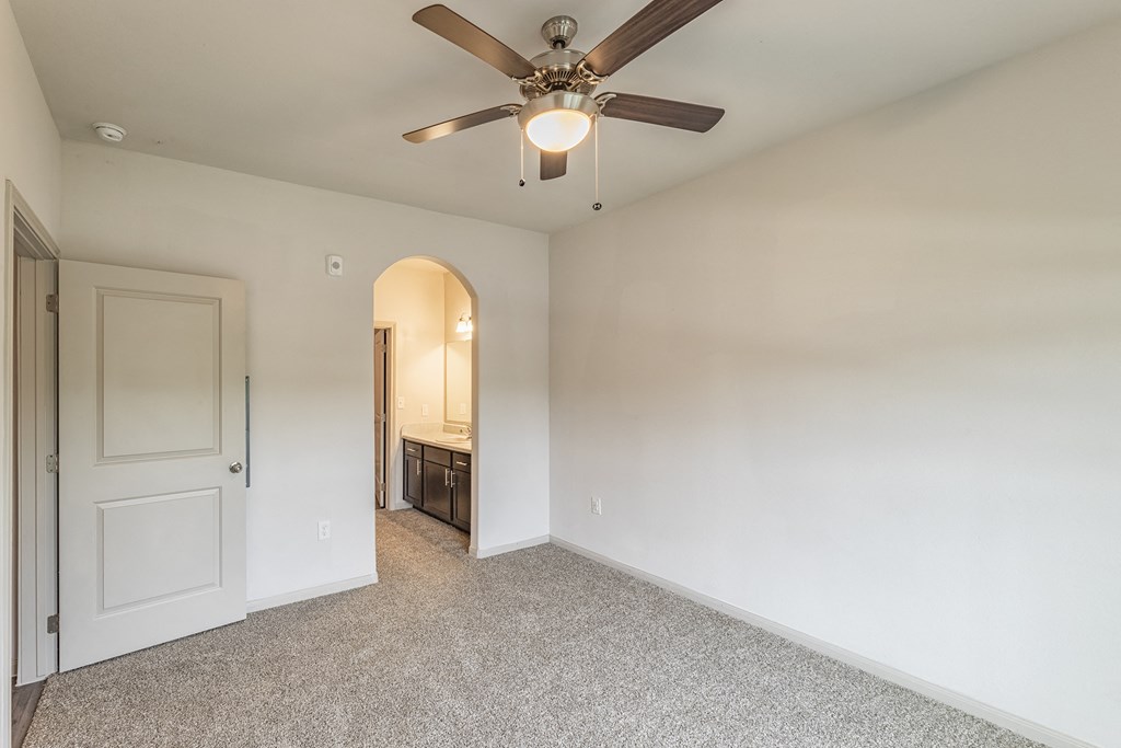 an empty room with a ceiling fan and a door to a bathroom
