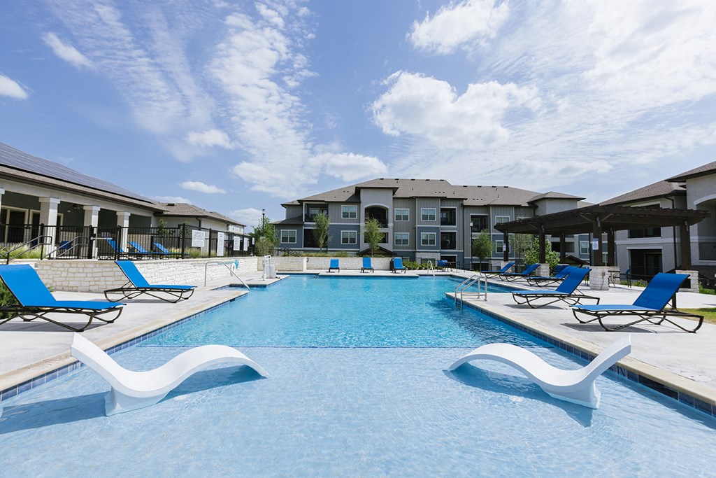 a swimming pool with blue chairs and buildings in the background