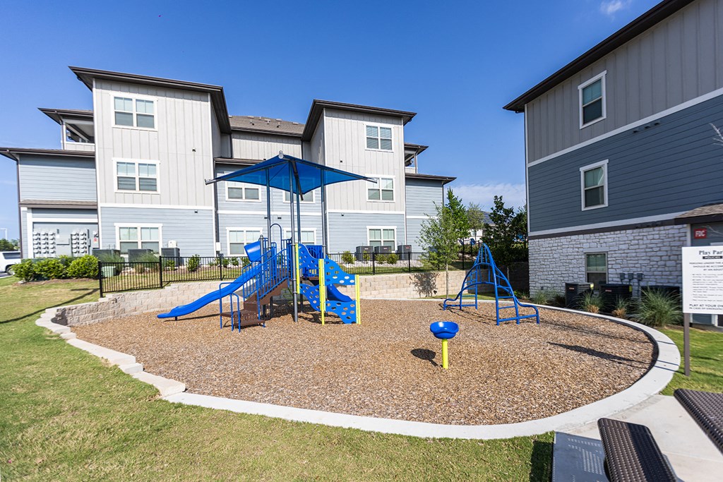 a playground with a blue swing set in front of apartments