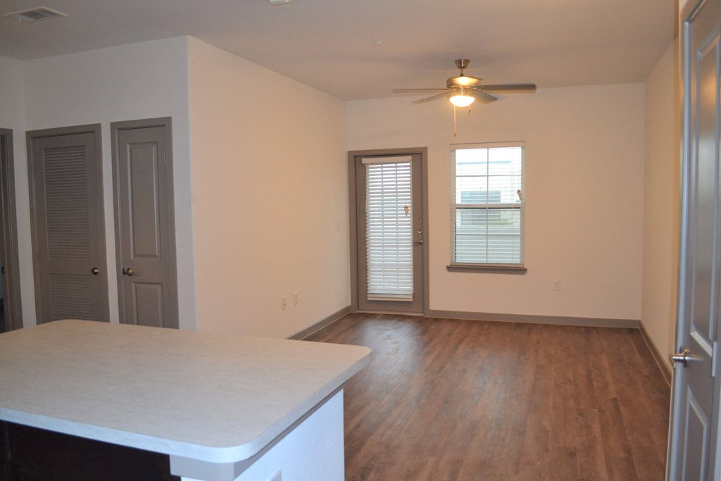 an empty living room with a kitchen and a ceiling fan