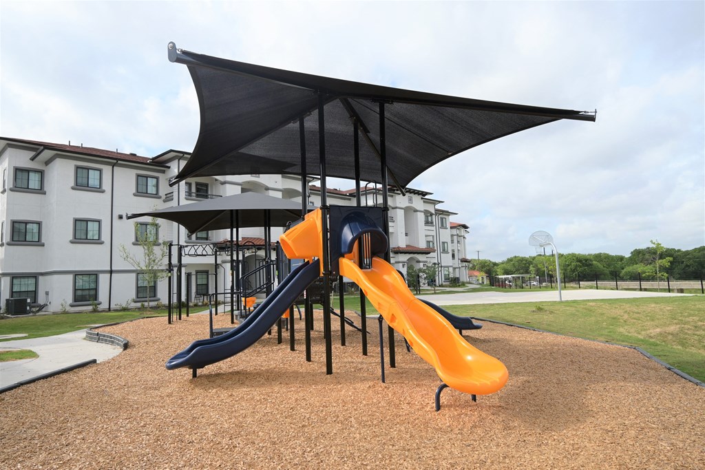 a playground with a slide and umbrella in front of a building