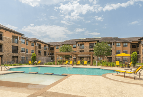 A swimming pool surrounded by yellow chairs and apartment buildings.
