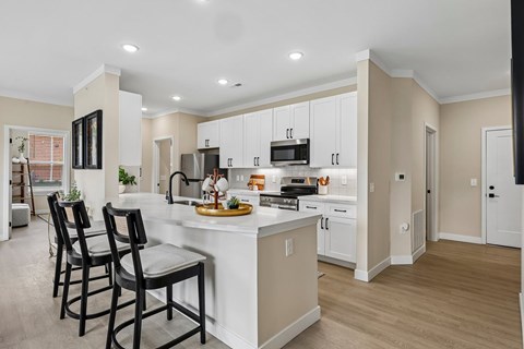 A kitchen with a white island and black chairs.
