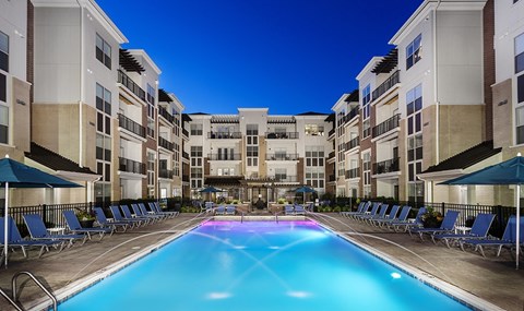A swimming pool in a residential area surrounded by lounge chairs and umbrellas.