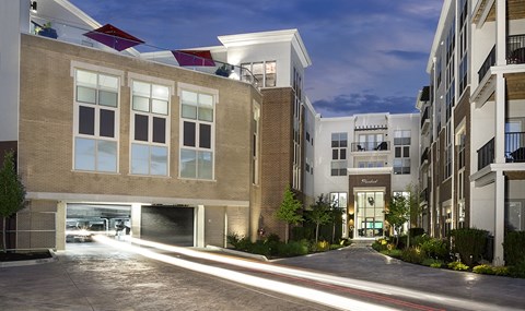 A modern apartment complex with a lit entrance and garage doors open.
