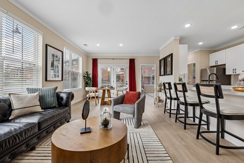 A living room with a black couch, a wooden coffee table, and a kitchen area in the background.