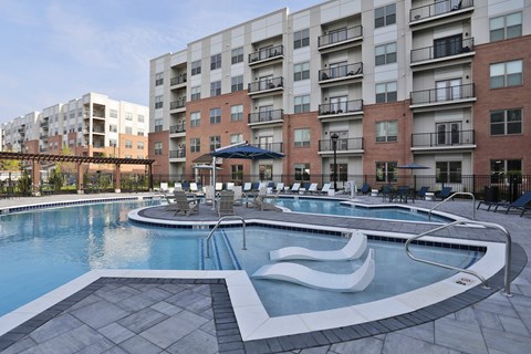 A large swimming pool with a slide in the middle is surrounded by apartment buildings.
