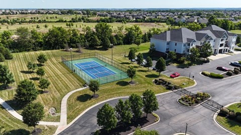 A tennis court is surrounded by a grassy area and a road.