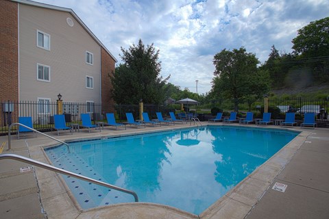 A large swimming pool surrounded by a metal fence and blue lounge chairs.