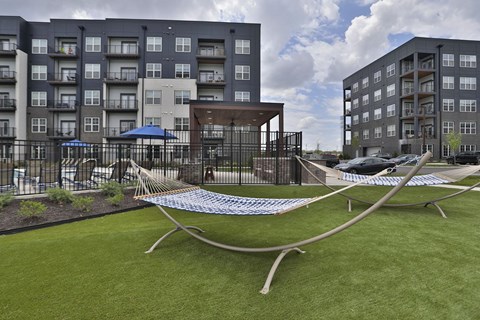 A hammock is strung between two poles in a grassy area in front of apartment buildings.