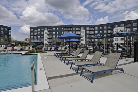 A pool area with sun loungers and umbrellas in front of apartment buildings.