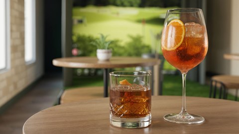 A glass of a drink with a slice of orange and a glass of a different drink with ice cubes on a table.