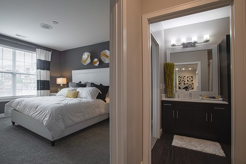 A bedroom with a large bed and a bathroom with a mirror and sink.