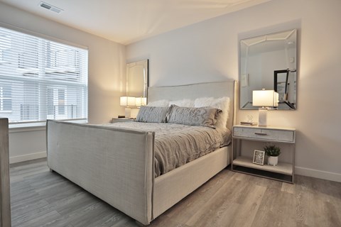 A bedroom with a large bed and a nightstand with a mirror above it.
