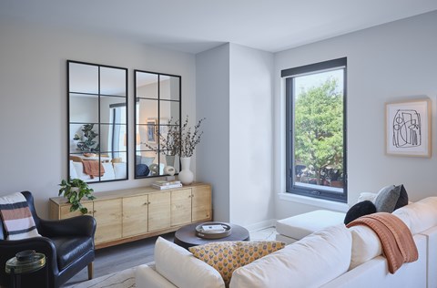 A living room with a white couch, a black chair, and a wooden cabinet with a mirror above it.