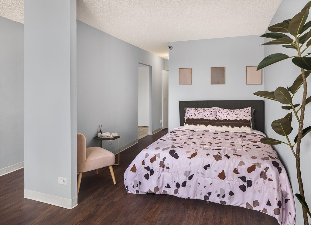 A bedroom with a bed, chair, and plant.