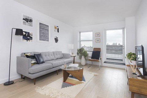 A living room with a grey couch, a coffee table, and a large window.