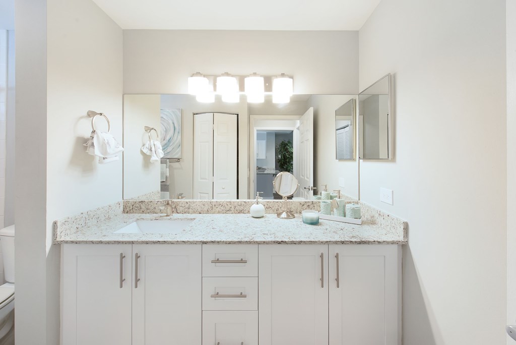 A bathroom with a marble countertop and white cabinets.