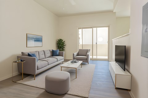 A living room with a grey sofa, a grey armchair, a grey ottoman, a coffee table, a flat screen TV, and a painting on the wall.