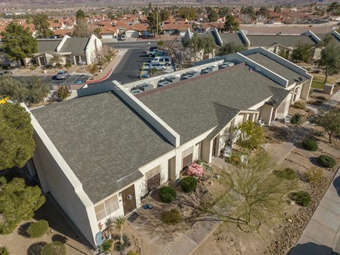 A large building with a grey roof is surrounded by trees and other buildings.
