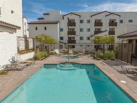 A swimming pool in a courtyard surrounded by chairs and buildings.