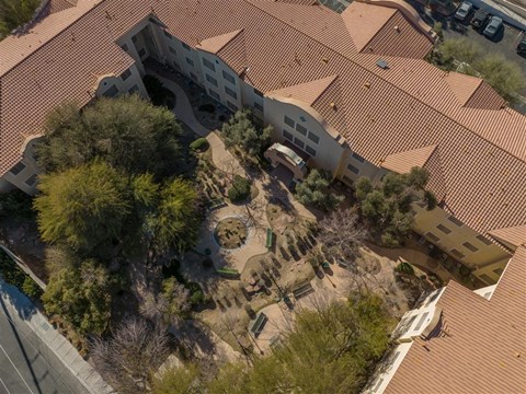 An aerial view of a building with a red tiled roof and a courtyard with trees and bushes.
