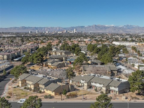 A residential area with houses and trees in the foreground and a city skyline with mountains in the background.