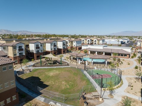 A park with a basketball court and a playground is surrounded by apartment buildings.