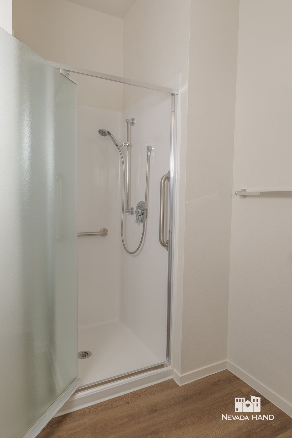 a small shower in a white room with a wood floor