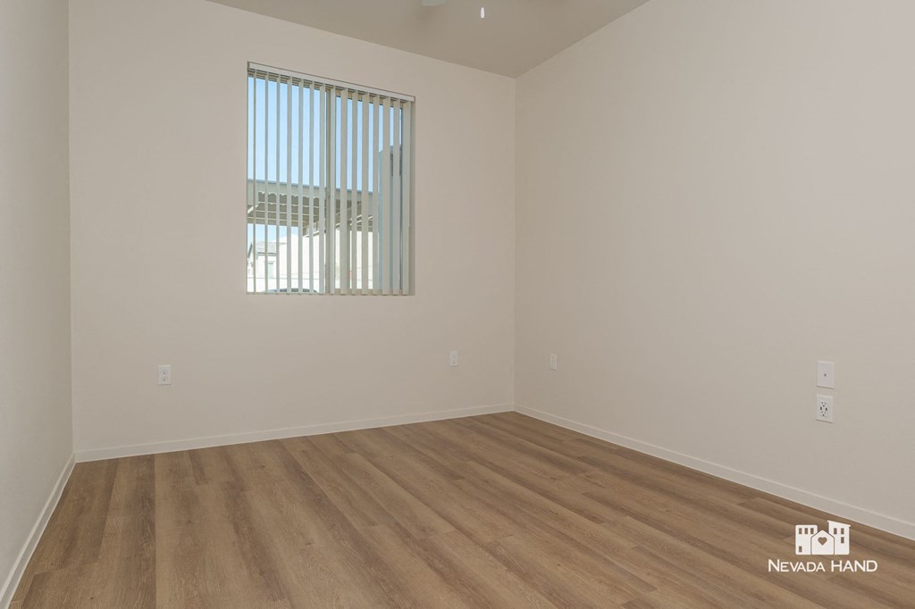 a bedroom with white walls and wood flooring and a window