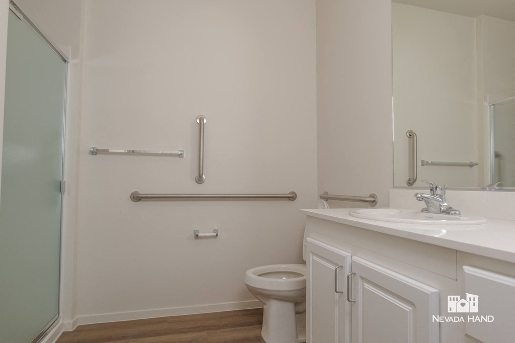 a white bathroom with grab bars and a toilet and sink