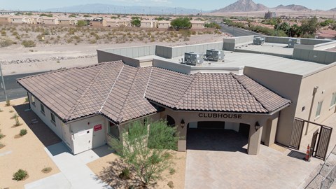 A clubhouse with a brown roof is surrounded by a parking lot and other buildings.