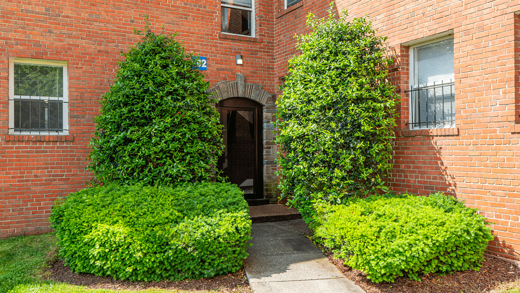 A red brick building with green bushes in front at Eagles Crossing Apartments, Washington DC