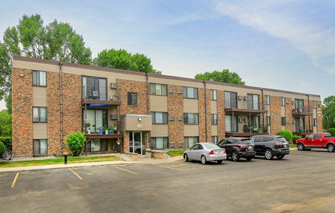 A parking lot in front of a brick apartment building with cars parked.