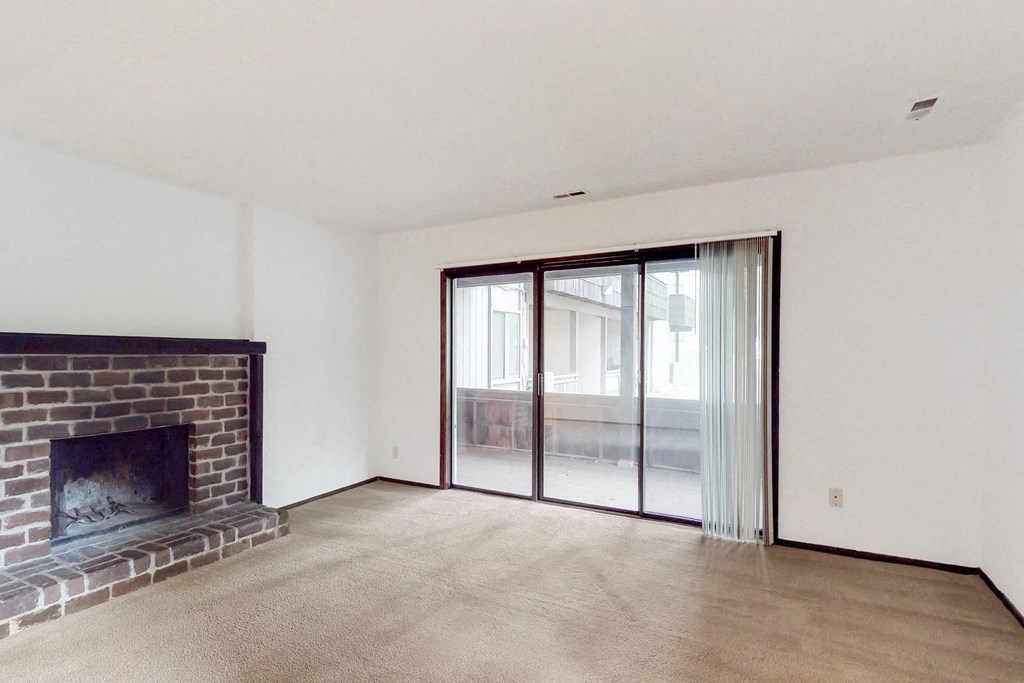 an empty living room with a brick fireplace and sliding glass doors