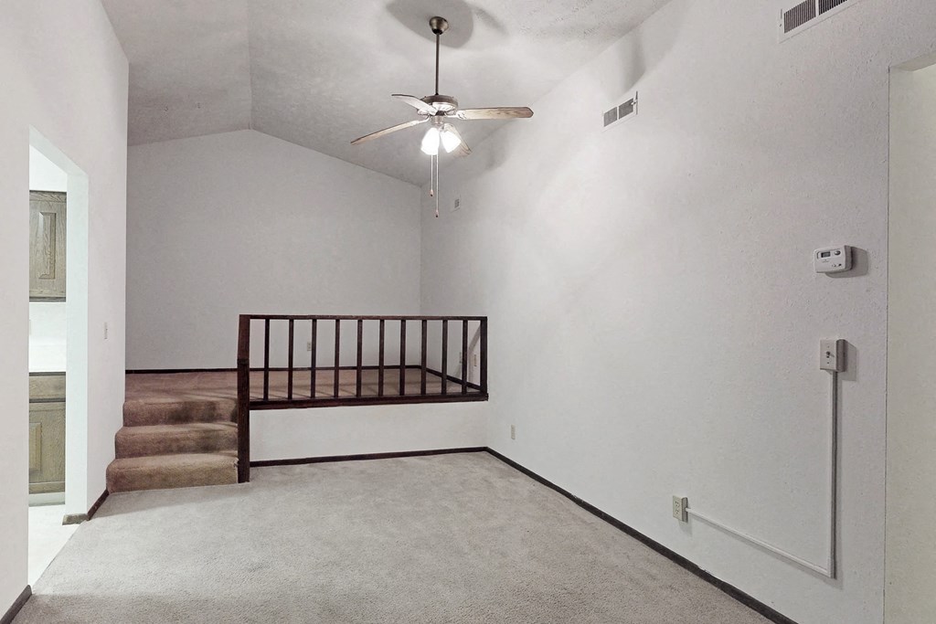 an empty living room with stairs and a ceiling fan