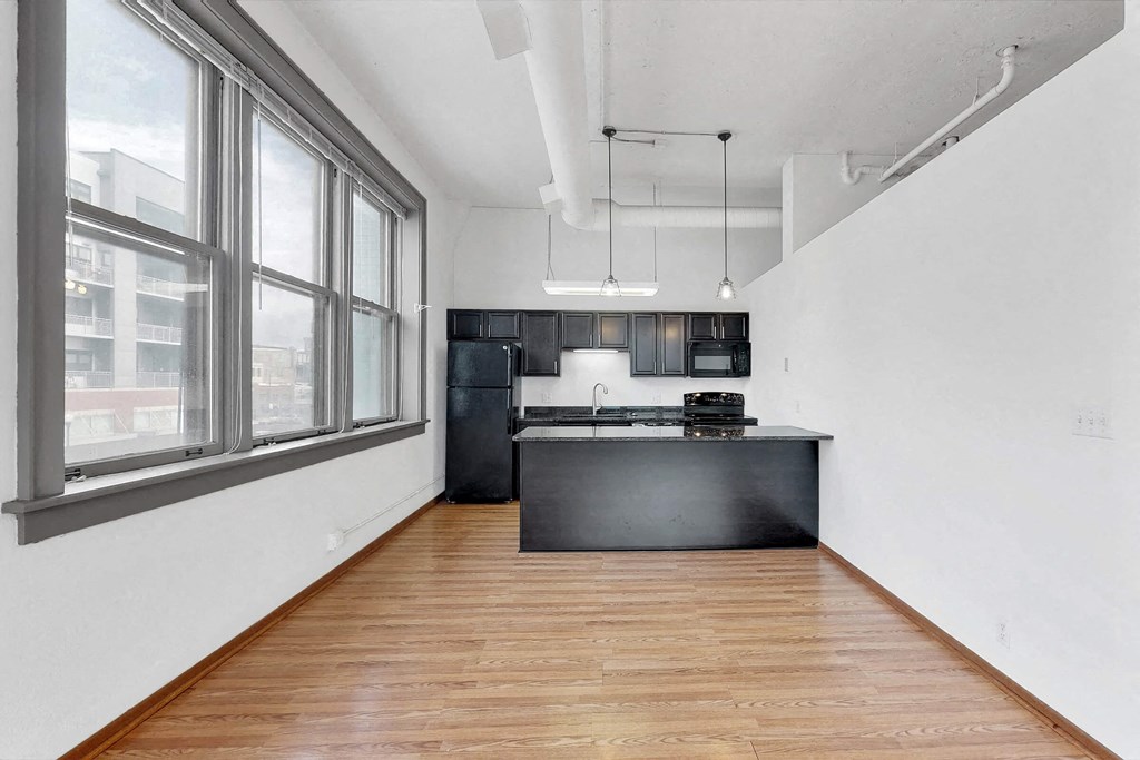 an empty living room with a large window and a kitchen
