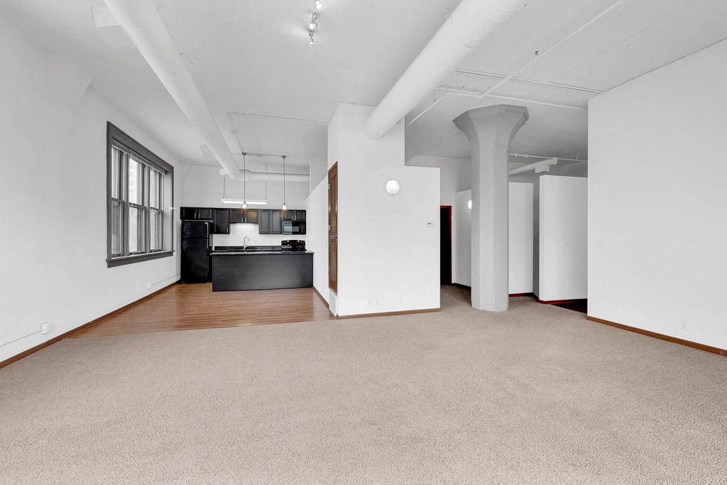 an empty living room with a kitchen in the corner