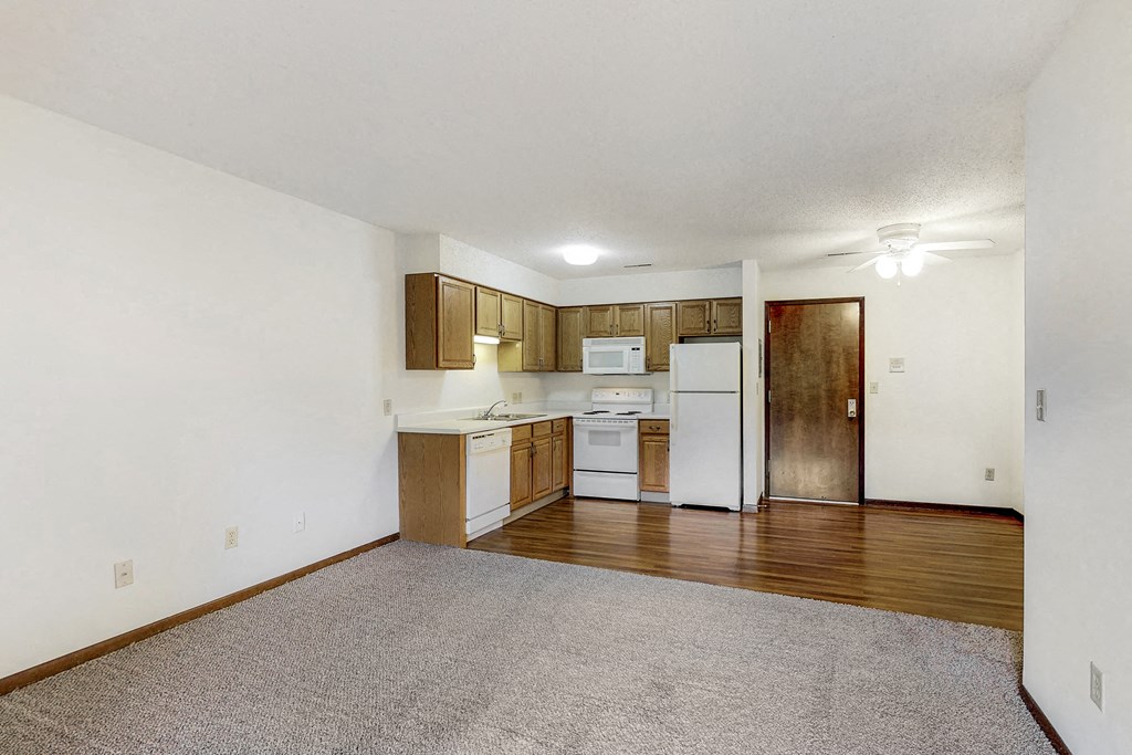 an empty living room and kitchen with wood floors and white appliances