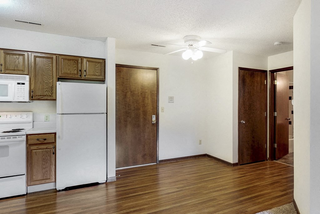 an empty kitchen with white appliances and wood flooring and a ceiling fan