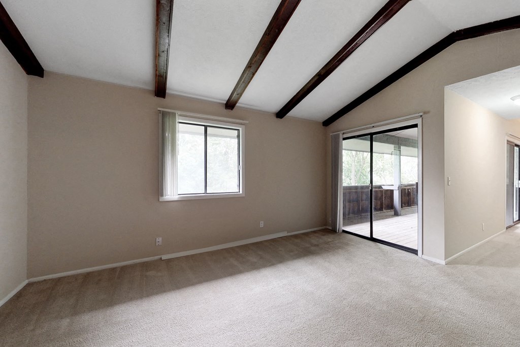 an empty living room with ceiling beams and a sliding glass door