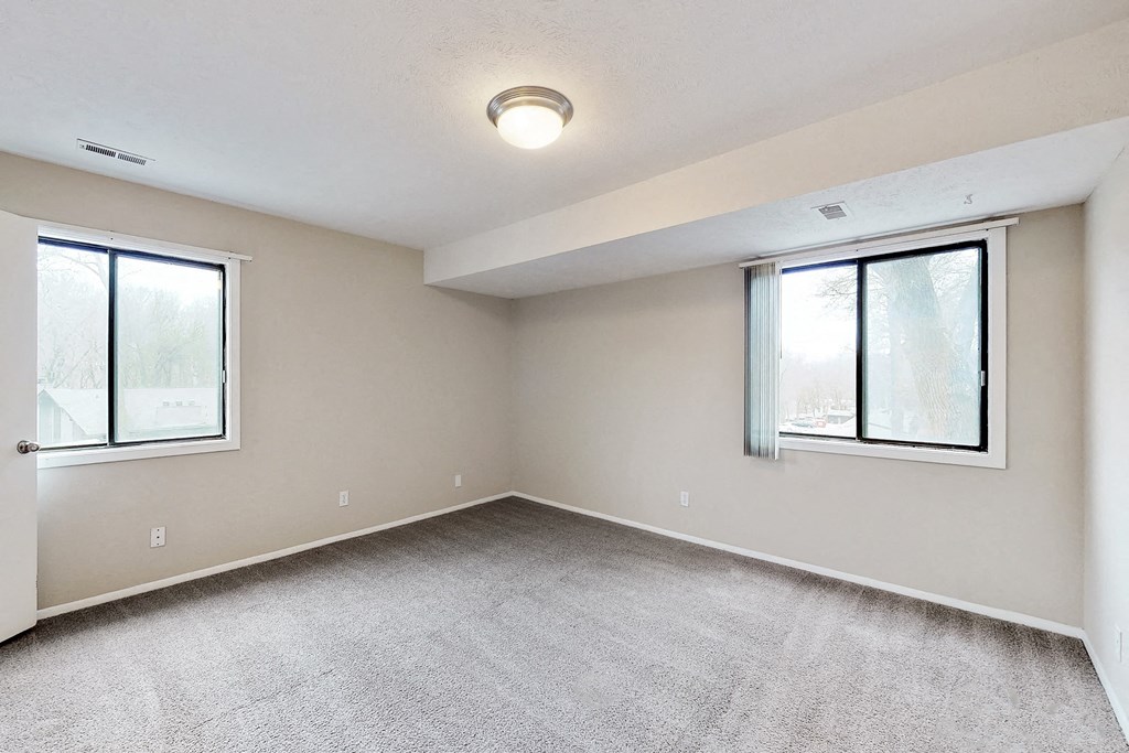 an empty living room with two windows and carpeting