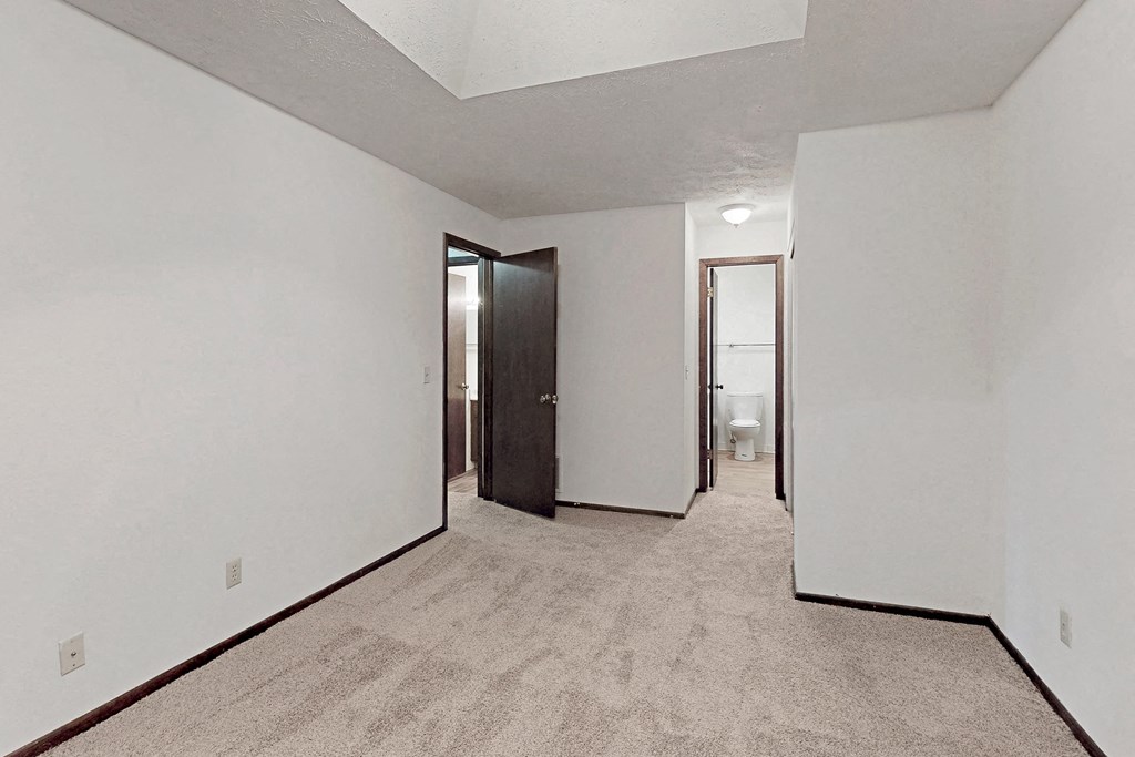 a room with white walls and a carpeted floor and a door to a bathroom