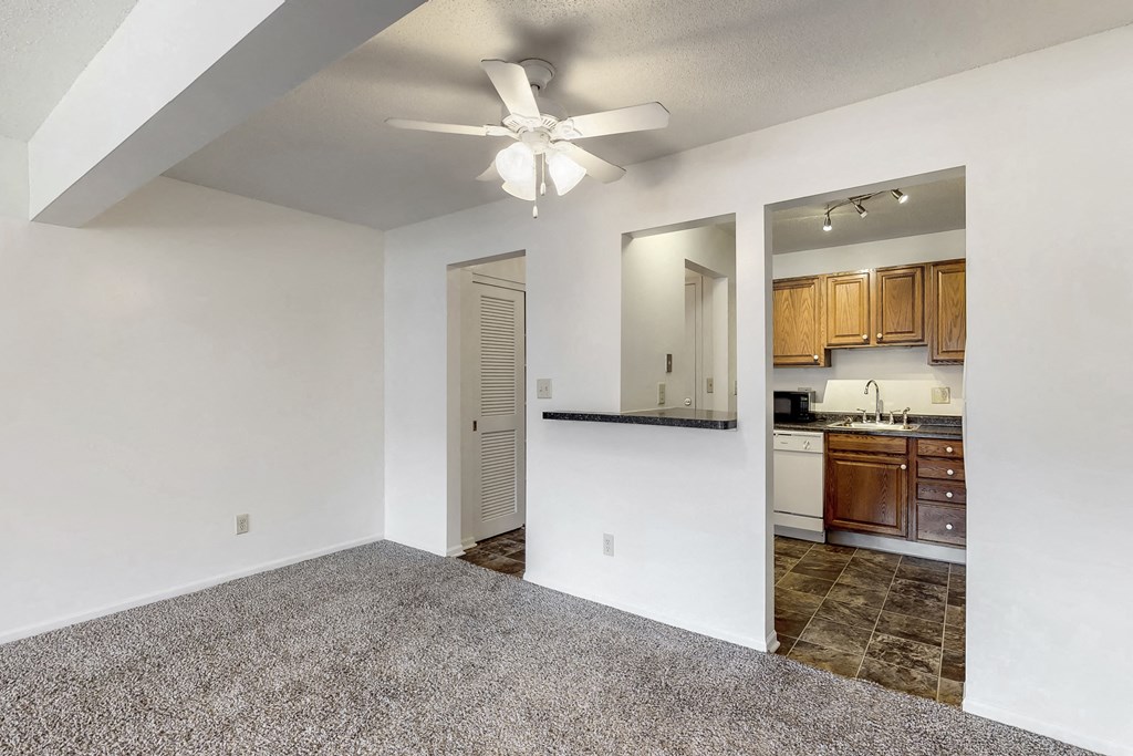 an empty living room with a ceiling fan and a kitchen