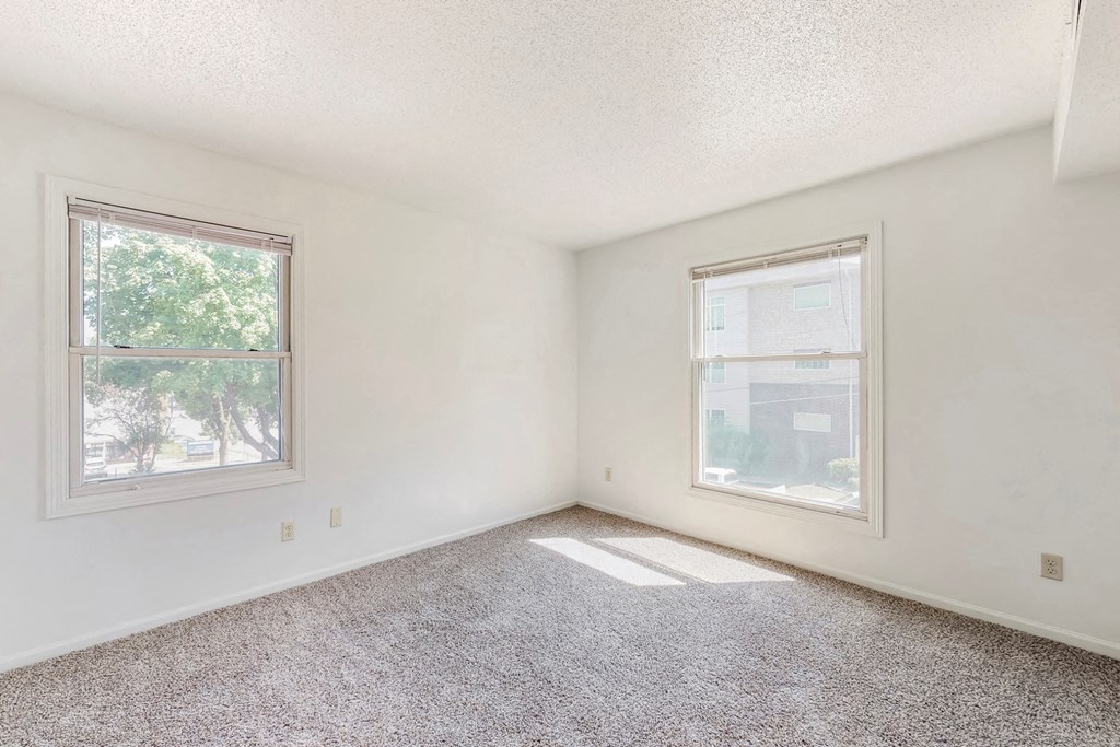 an empty bedroom with two windows and a carpeted floor